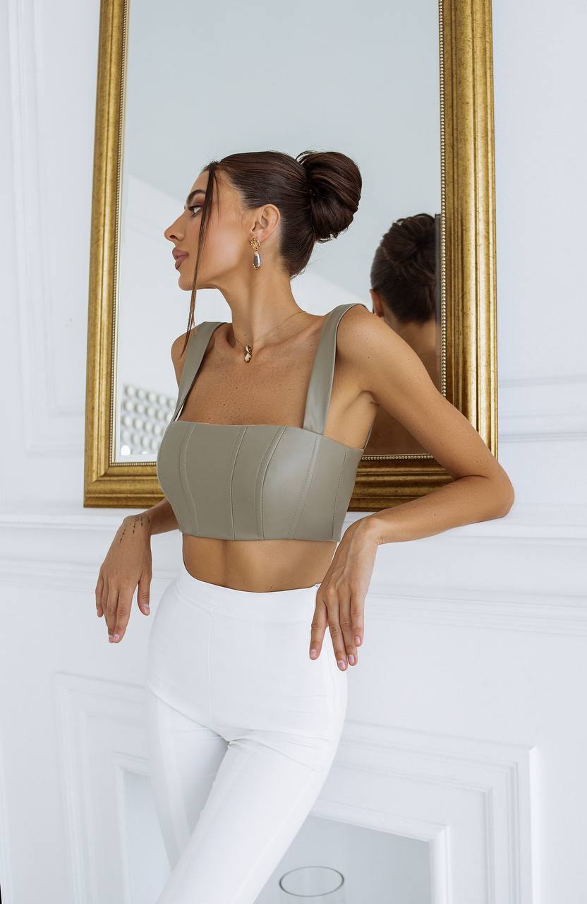 Woman wearing a green sports bra and white leggings standing in front of a mirror.