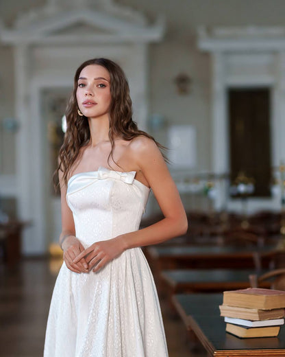 Woman in a white strapless dress with a bow tie standing in an elegant room.