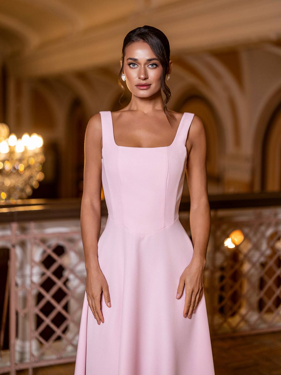 Woman wearing a pink dress in an elegant indoor setting with chandeliers.