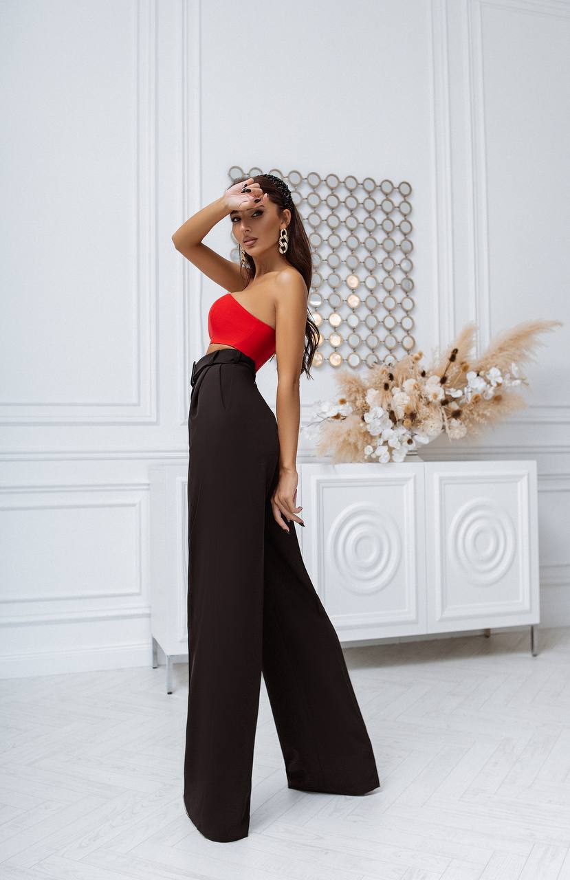 Woman in a red top and black pants posing in a stylish interior setting.