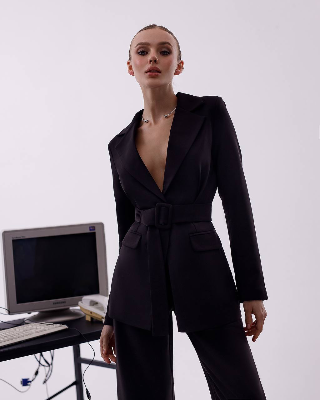 Person wearing a black suit standing next to a vintage computer setup on a white background