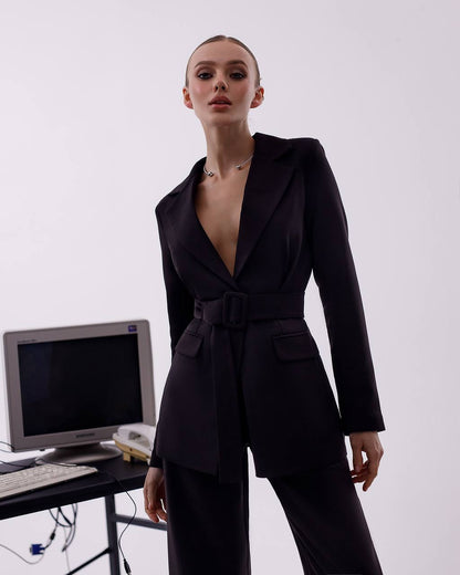 Person wearing a black suit standing next to a vintage computer setup on a white background
