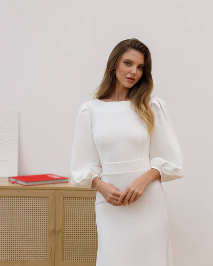 Woman in a white dress standing in an indoor setting with a neutral background
