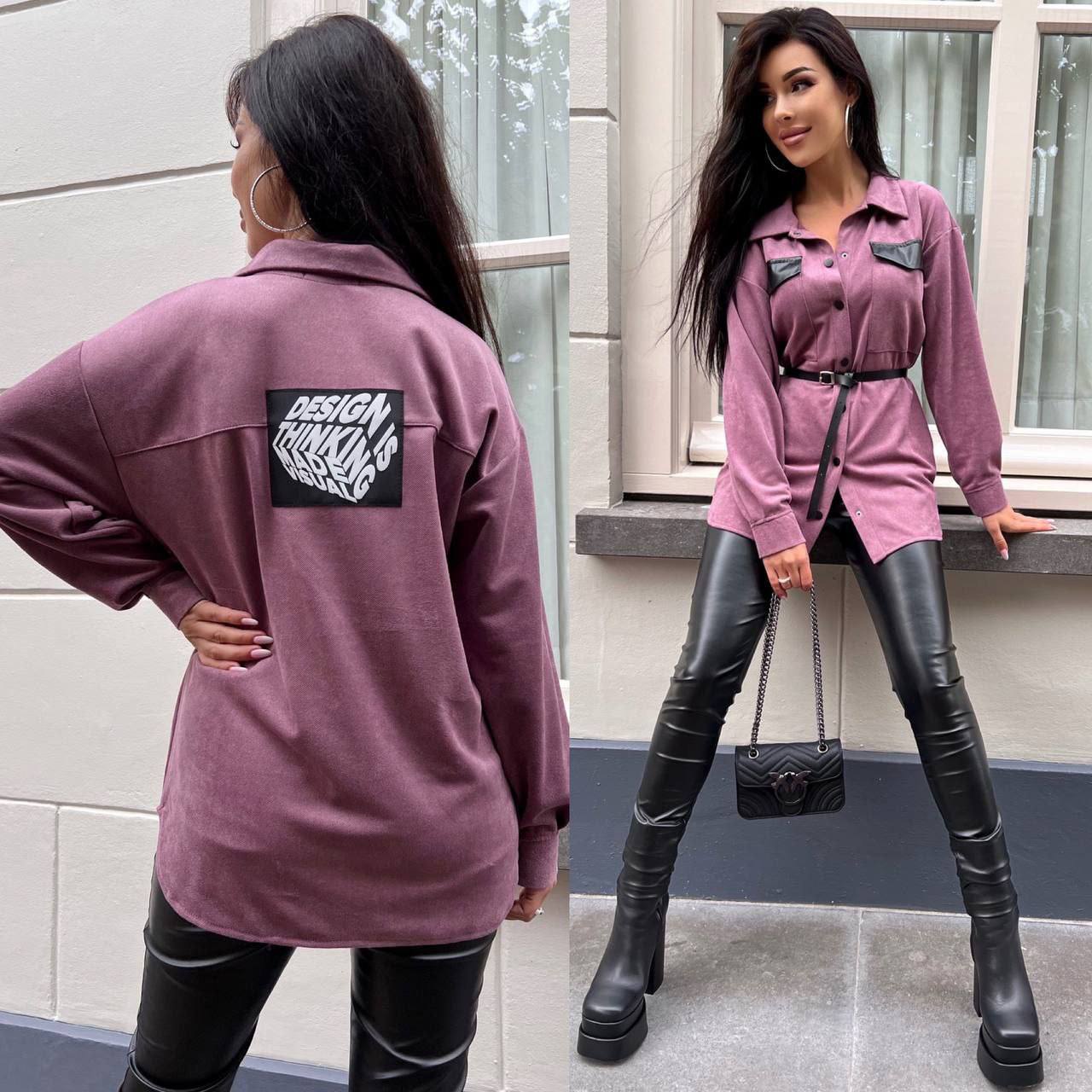 Woman wearing a purple jacket with a brand logo and black leather pants, standing against a building exterior.