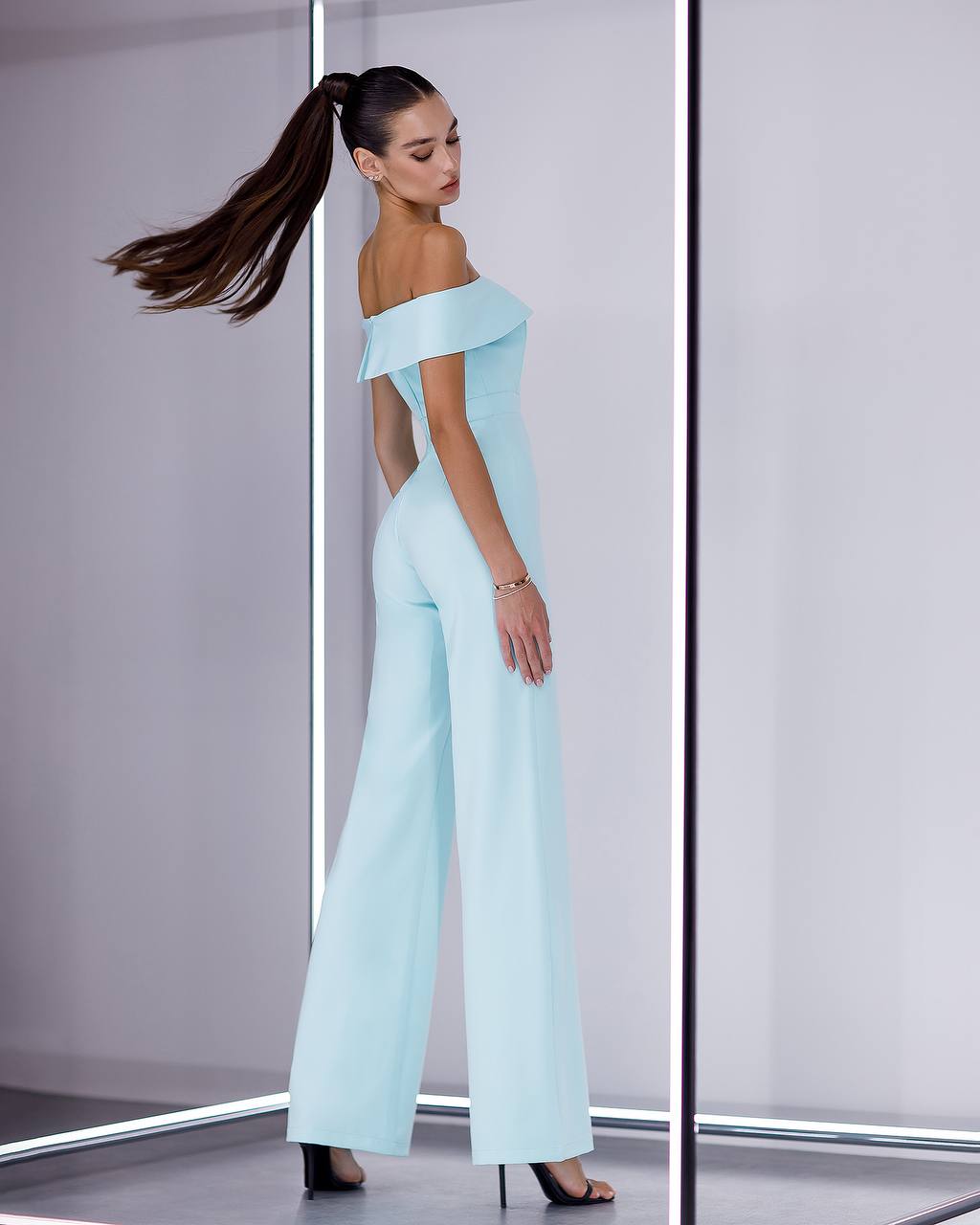 Woman wearing a light blue off-shoulder jumpsuit in a minimalistic setting