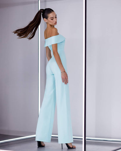 Woman wearing a light blue off-shoulder jumpsuit in a minimalistic setting