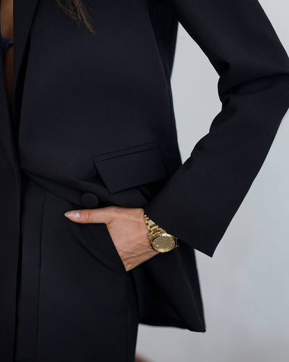 Person wearing a black coat with a gold watch on a plain background