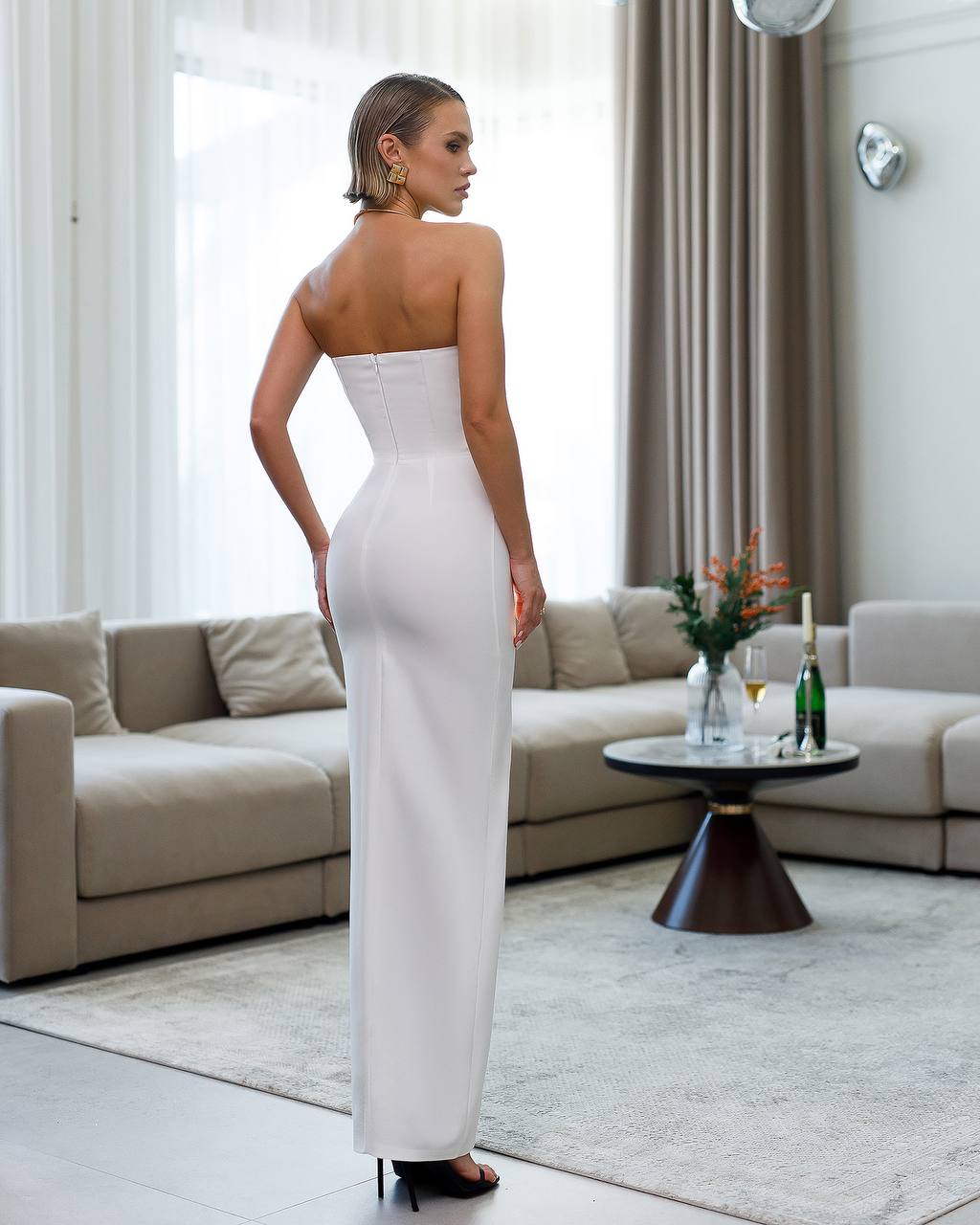 Woman in a white strapless dress standing in a modern living room.
