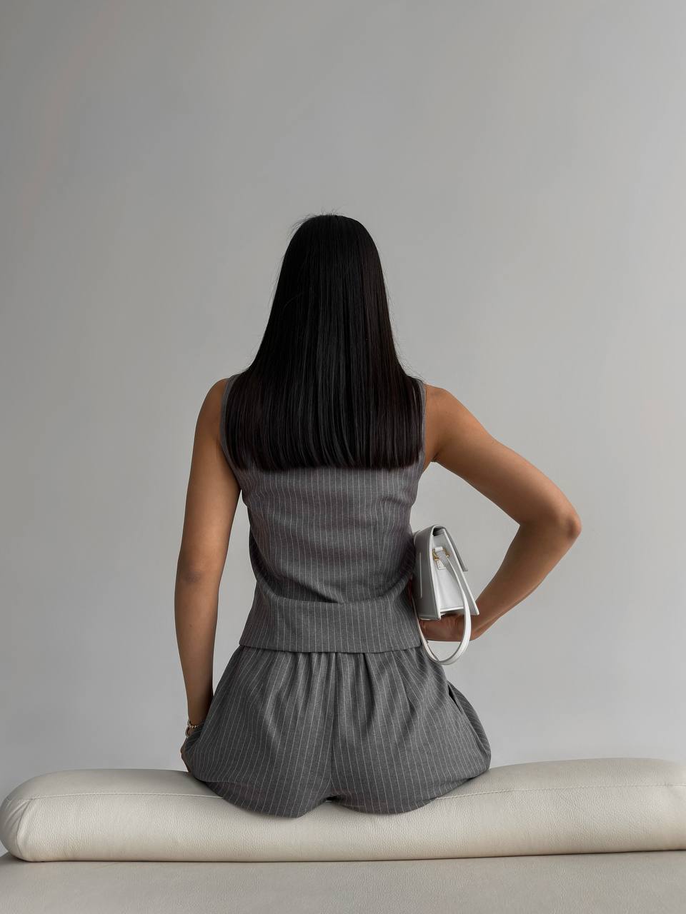Person wearing a gray sleeveless dress sitting on a white bench against a plain background