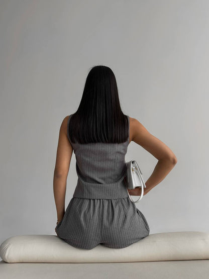 Person wearing a gray sleeveless dress sitting on a white bench against a plain background