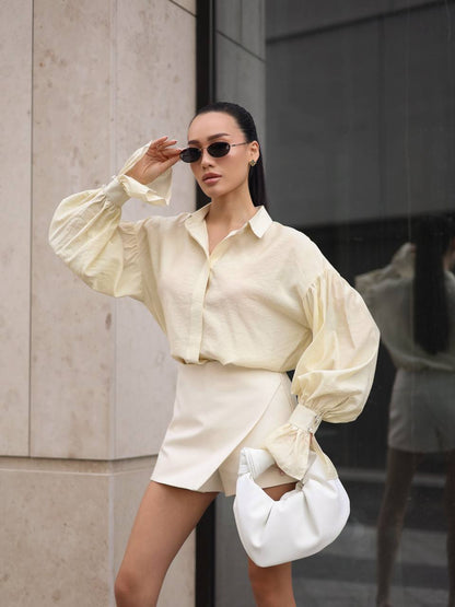 Woman in a cream-colored outfit with a white handbag standing against a building.