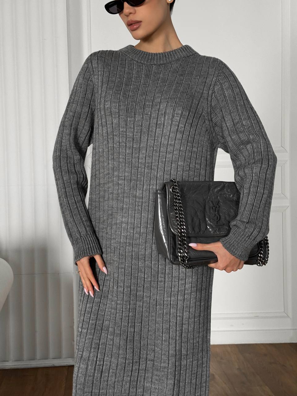 Person wearing a gray ribbed dress holding a black handbag indoors.