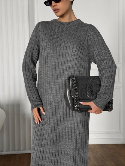 Person wearing a gray ribbed dress holding a black handbag indoors.