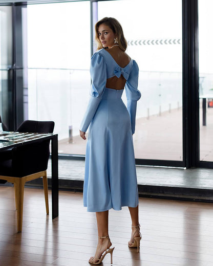 Woman in a light blue dress standing in a modern room with large windows.
