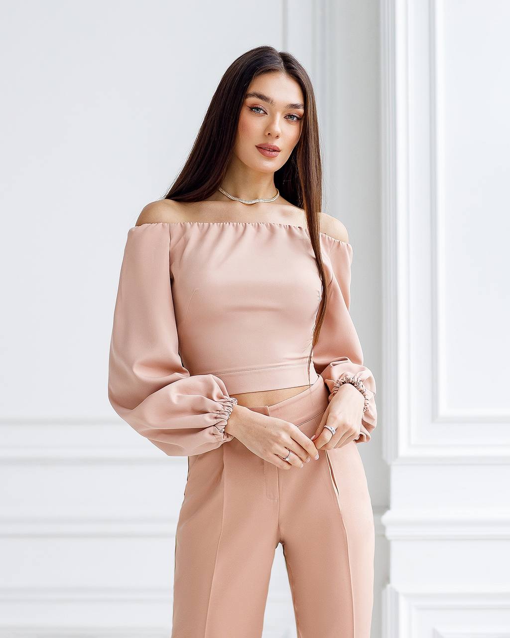 Woman wearing a pink off-shoulder top and pants against a white wall