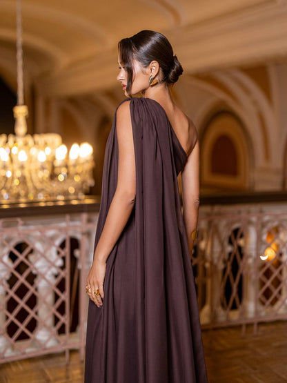 Woman in a brown dress standing in an elegant indoor setting with chandeliers.