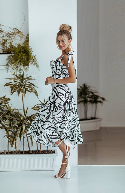 Woman in a black and white patterned dress standing in a room with plants.