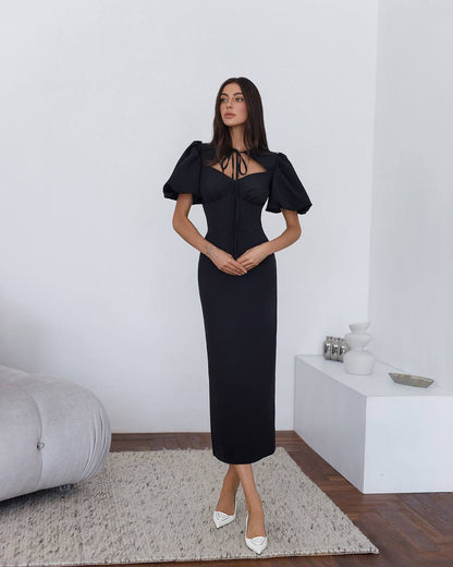 Woman wearing a black dress with puffed sleeves in a minimalistic room.