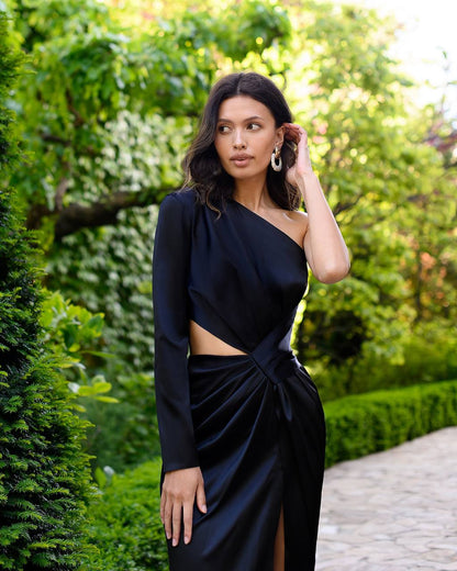 Woman in a black one-shoulder outfit standing in a garden