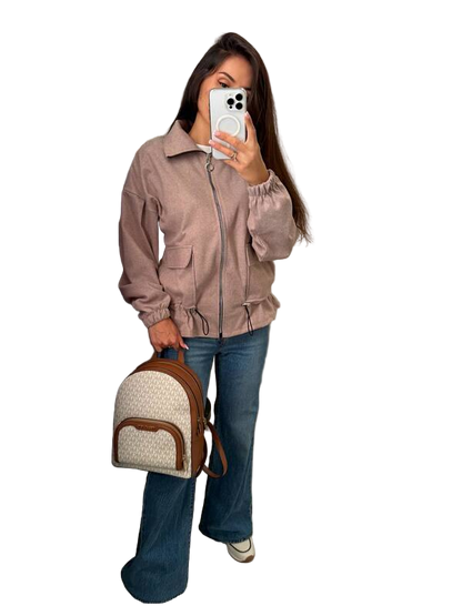 Woman holding a phone and a backpack, wearing a beige jacket and blue jeans on a white background