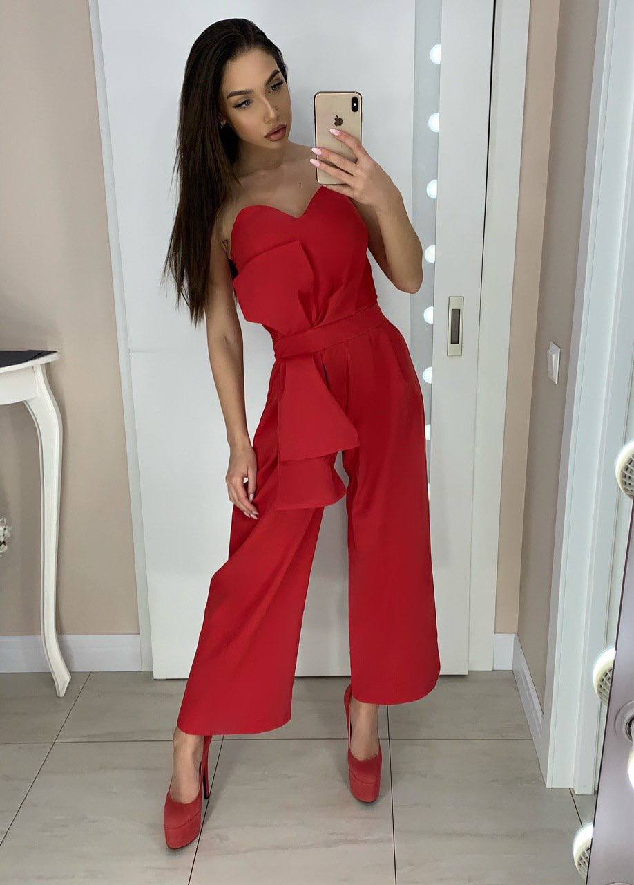 Woman taking a mirror selfie wearing a red strapless jumpsuit and high heels.