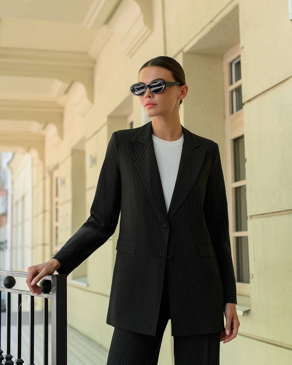 Person wearing a black pinstripe suit and sunglasses in front of a building.