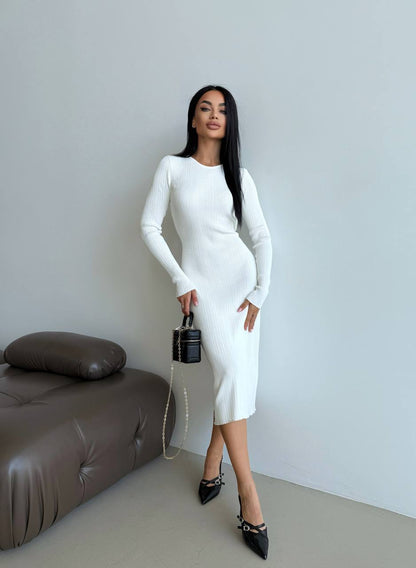 Woman in a white dress holding a black handbag in a minimalistic room.