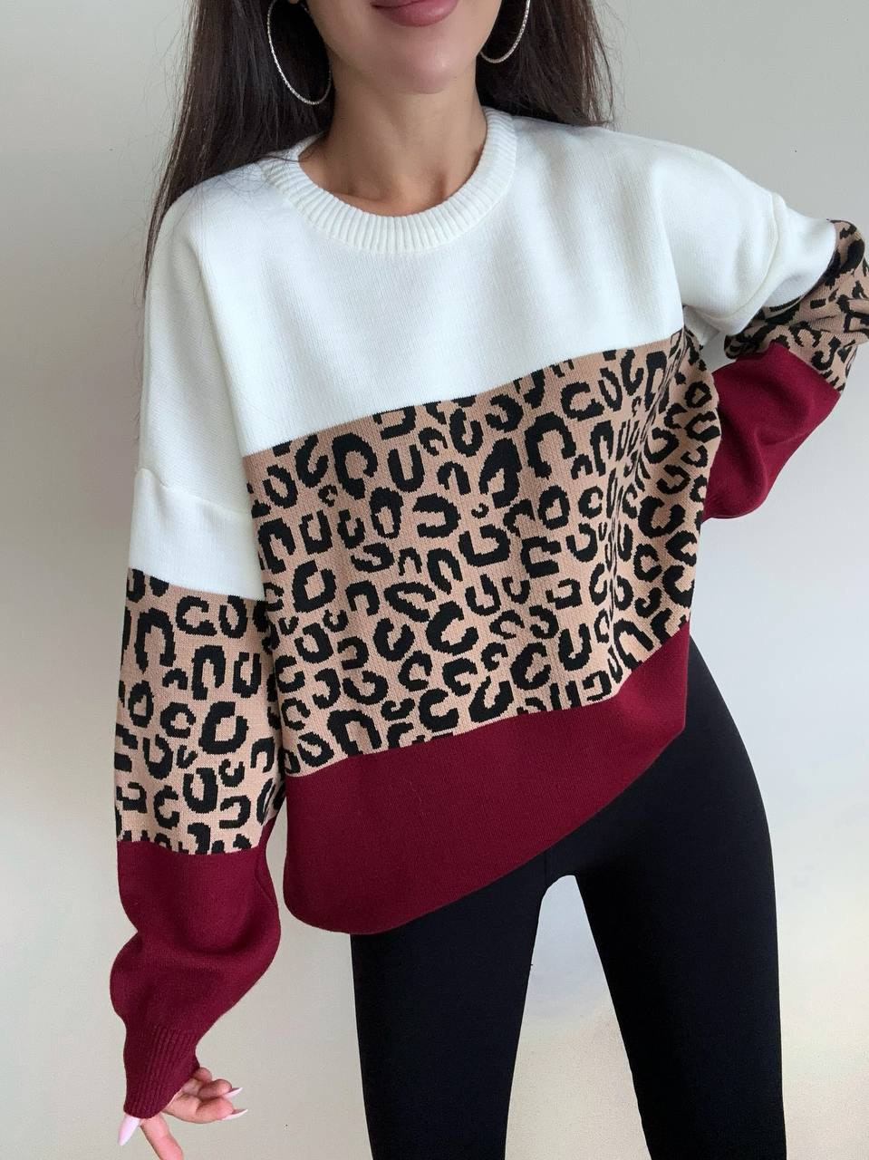 Person wearing a white sweater with leopard print and red sections on a plain background