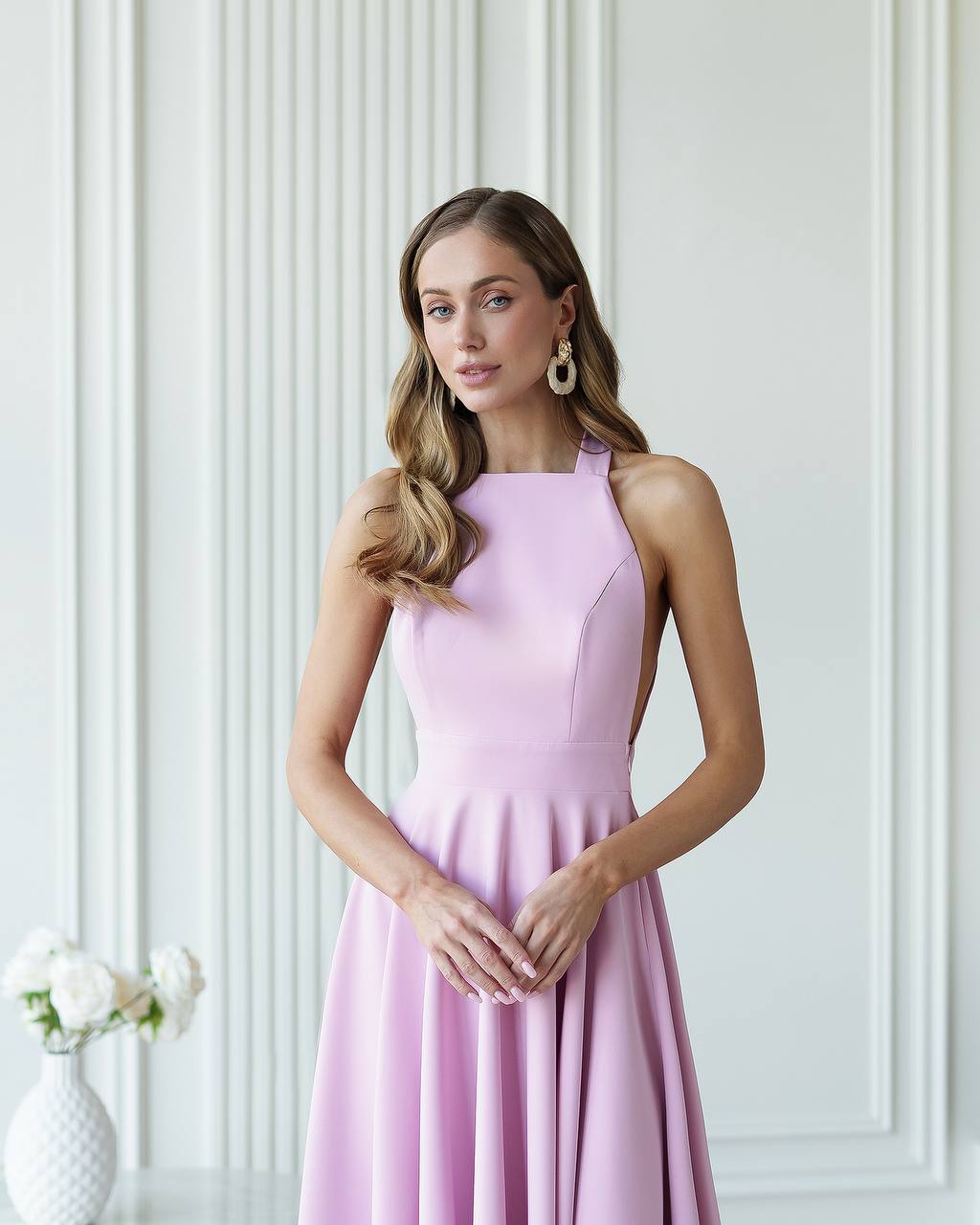 Woman wearing a pink dress standing against a white paneled wall.