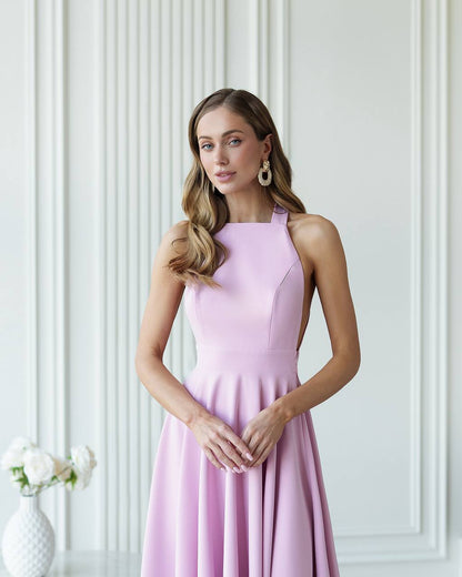 Woman wearing a pink dress standing against a white paneled wall.