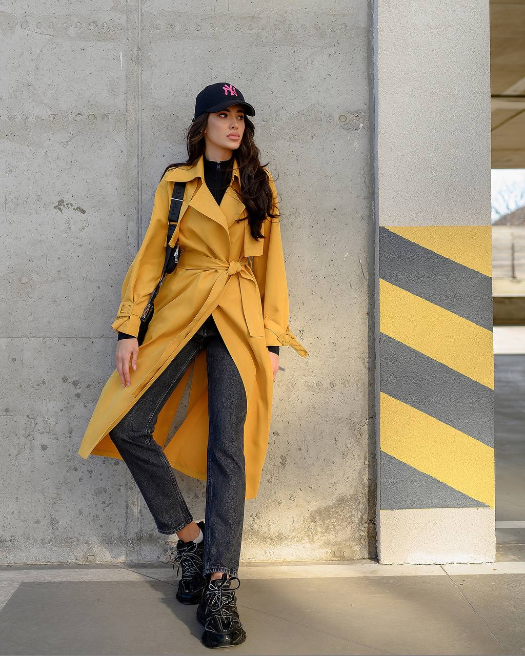 Person wearing a yellow trench coat standing against a concrete wall with yellow and gray striped pattern.