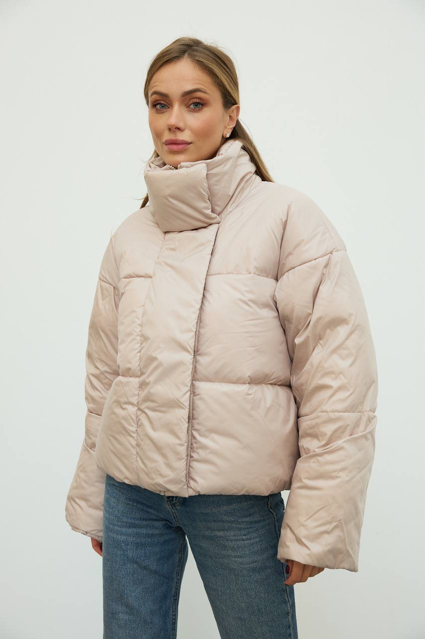 Woman wearing a beige puffer jacket against a white background