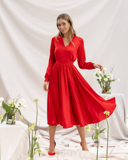 Woman wearing a red dress with long sleeves in a minimalistic setting.