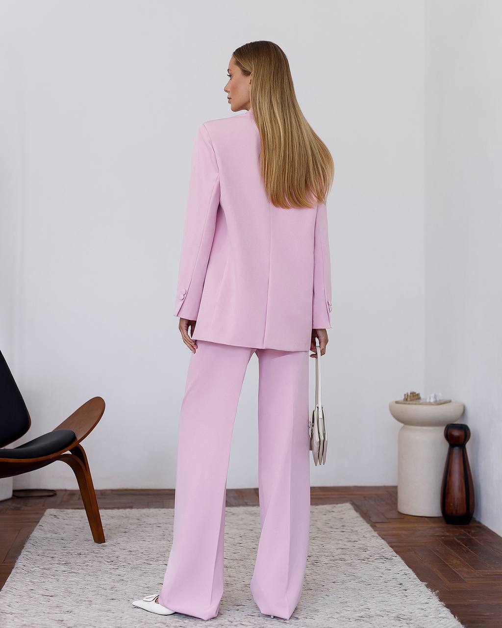 Woman wearing a pink suit standing in a minimalistic room.
