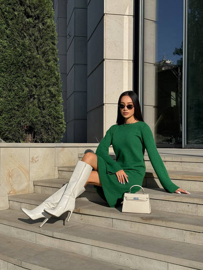 Woman in a green dress and white knee-high boots sitting on steps outdoors.