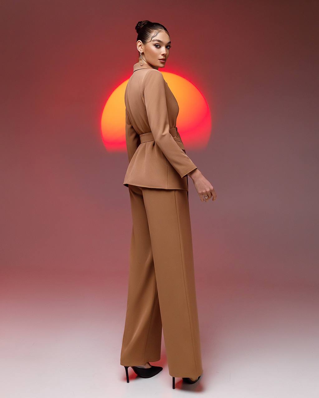 Woman in a brown suit standing against a sunset background