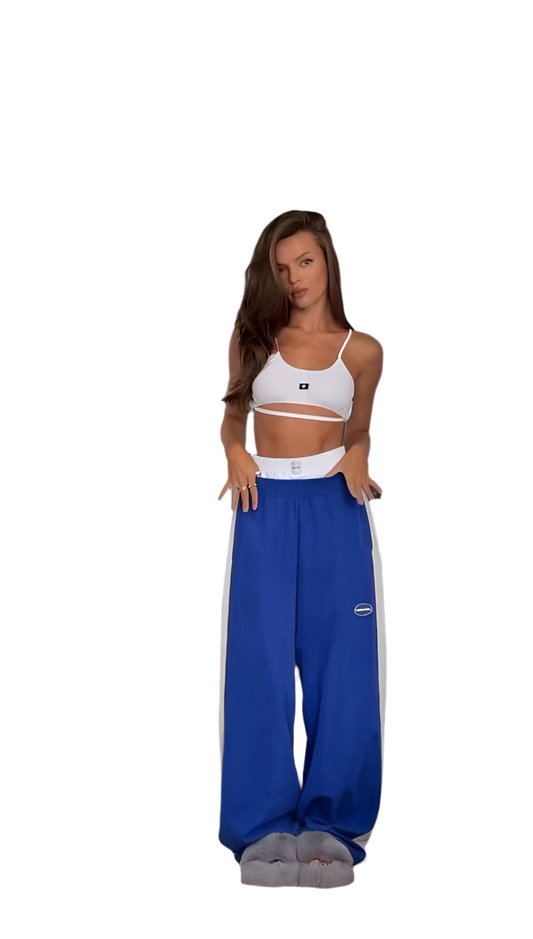 Woman wearing a white sports bra and blue sweatpants with a brand logo on a white background