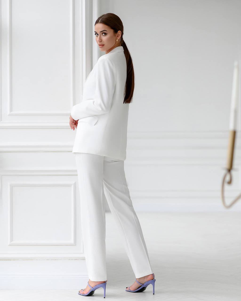 Woman in a white suit standing against a white wall
