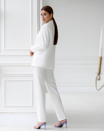 Woman in a white suit standing against a white wall
