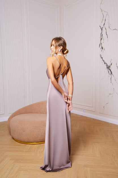 Woman in a long, elegant dress standing in a room with a marble wall.