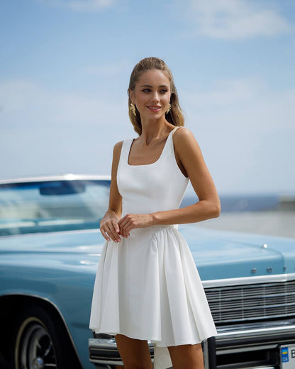 Woman in a white dress standing next to a vintage car with a clear sky background