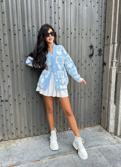 Woman wearing a light blue cardigan with a pattern, white skirt, and white sneakers in front of a metallic door.