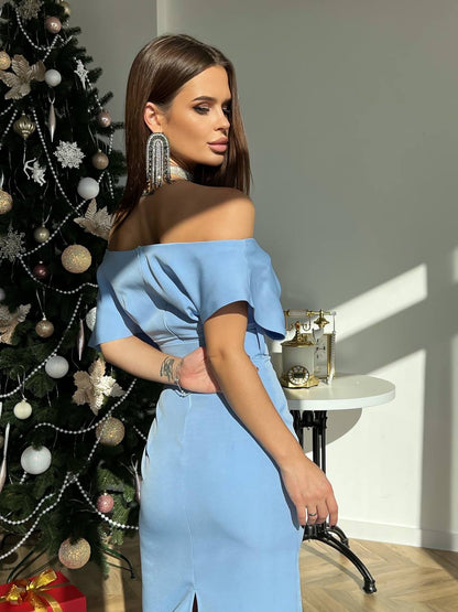 Woman in a blue off-shoulder dress standing next to a decorated Christmas tree.