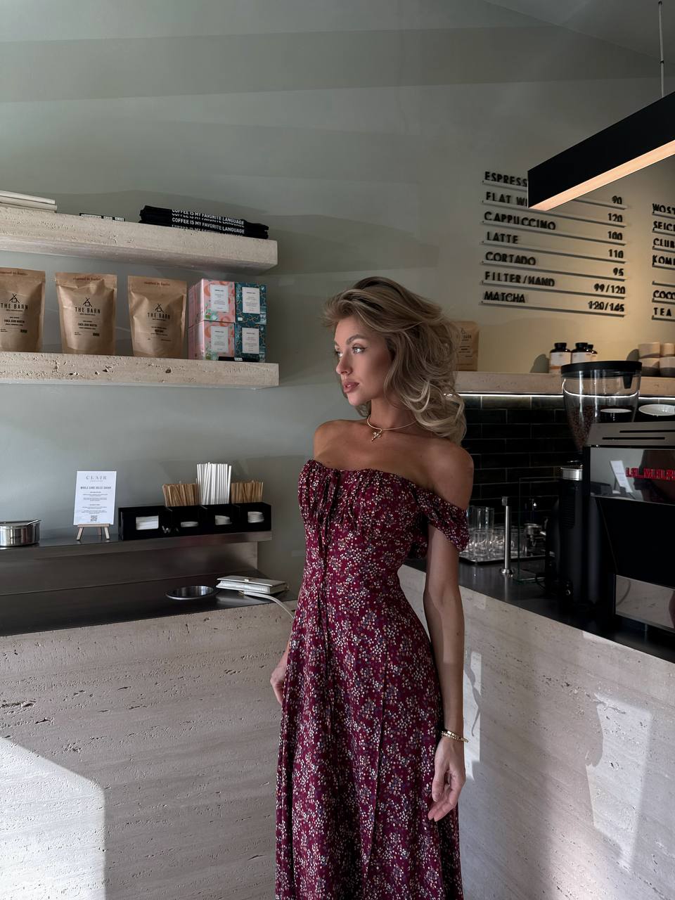 Woman in a floral dress standing in a coffee shop.