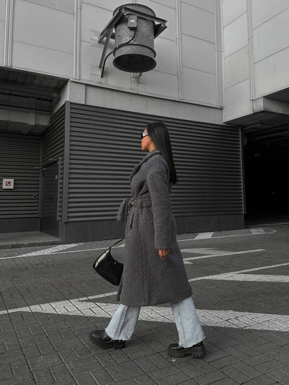 Person wearing a long coat walking on a street with a building in the background