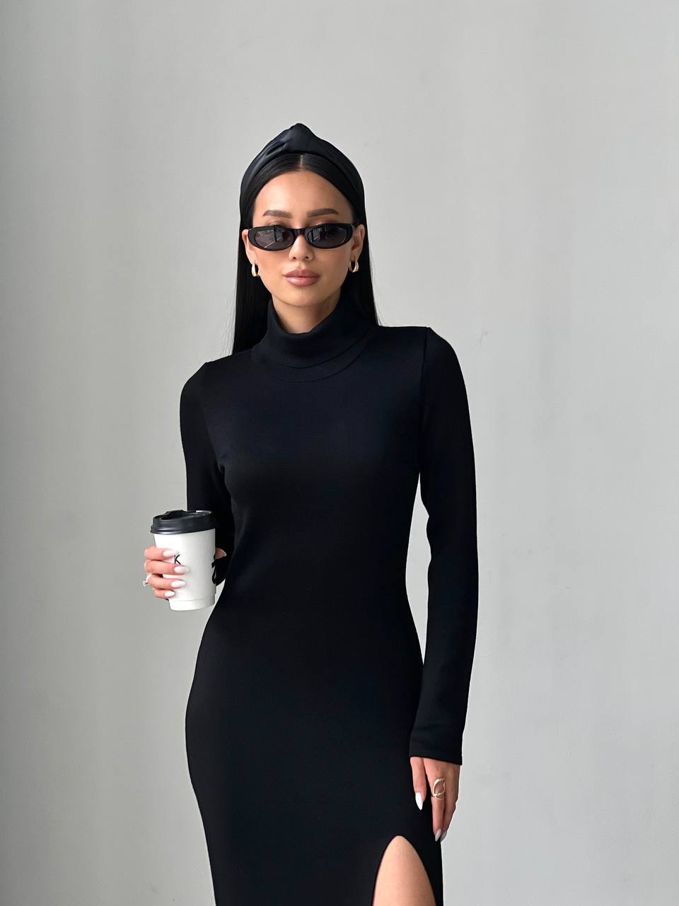 Woman in a black dress and headscarf holding a coffee cup against a gray background