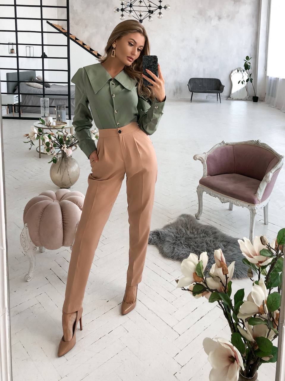 Woman taking a mirror selfie in a stylish outfit in a modern living room.