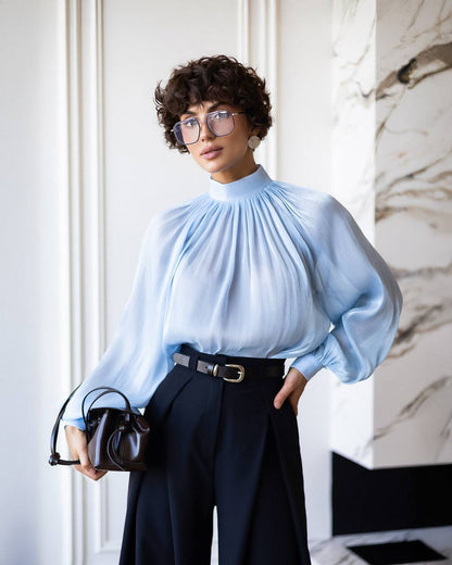 Person wearing a light blue blouse and dark pants in an indoor setting