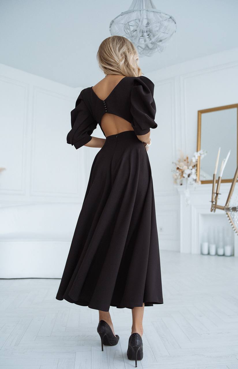 Woman wearing a black dress with a backless design in a white room.