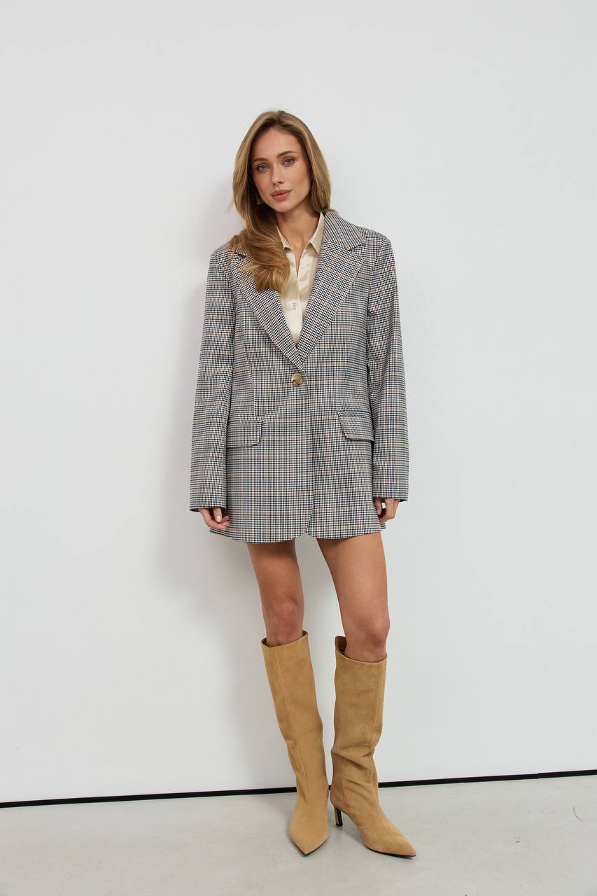 Woman wearing a gray checkered blazer dress with beige knee-high boots against a white background